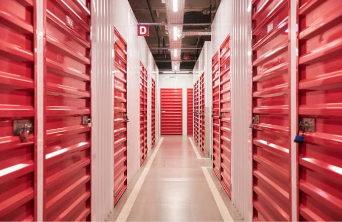 Row of secure self storage units with red locked doors inside a clean indoor storage facility